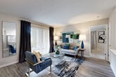 This thoughtfully designed single-floor residence offers a bright and welcoming open-concept layout that seamlessly connects the living, dining, and kitchen areas. The living room features wood-style plank flooring, large sliding glass doors dressed with floor-to-ceiling drapes, and direct access to a private balcony overlooking lush greenery. The kitchen is outfitted with white cabinetry, a white quartz peninsula countertop, a tile backsplash, and a full suite of stainless steel appliances including a gas range, microwave, and refrigerator. A dedicated dining area sits adjacent to the kitchen, completing the open living space. Both bedrooms are carpeted for comfort and include ceiling fans and ample natural light from well-placed windows. The primary bedroom connects directly to a bathroom featuring white cabinetry, a quartz vanity countertop, and a wood-framed mirror. A second full bathroom offers a tub-shower combination with clean, neutral finishes. A dedicated in-unit laundry room accommodates a full-size washer and dryer with additional shelving for storage. Throughout the residence, a neutral color palette and consistent finishes create a cohesive, modern ambiance.