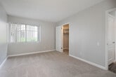 Located at 1101 W Stevens Ave in Santa Ana, California, this single-floor unit offers a well-organized layout designed for comfortable everyday living. The kitchen stands out as one of the most updated areas of the home, featuring crisp white cabinetry, speckled stone-look countertops, wood-look flooring, recessed lighting, and a full suite of stainless steel appliances including a refrigerator, electric range, microwave, and dishwasher. The galley-style configuration maximizes storage and counter space efficiently. The living area is bright and open, with large corner windows dressed in vertical blinds that allow generous natural light to fill the carpeted space. A wall-mounted HVAC unit provides climate control. The bedroom areas are equally well-appointed, featuring plush carpet flooring, neutral gray walls, and ample built-in closet space with shelving. The bathroom includes a full-size soaking tub and shower combo with clean white surrounds, a toilet, and a vanity with stone-look countertop. Crown molding details and textured ceilings are present throughout the living spaces, adding subtle architectural character. Overall, the unit presents a clean, neutral palette that provides a versatile backdrop for a variety of interior styles.