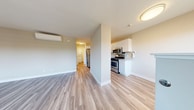 This thoughtfully designed 1-bedroom, 1-bathroom residence offers a comfortable and efficient single-floor layout. Light-toned laminate flooring runs consistently throughout the home, creating a cohesive and clean aesthetic. The open living area features a wall-mounted mini-split climate control unit and flows naturally toward the kitchen, which is outfitted with stainless steel appliances including a gas range, microwave, and refrigerator. White shaker-style cabinetry and built-in open shelving provide ample storage, complemented by a neutral countertop and a stainless steel sink. The bedroom is a well-proportioned private retreat featuring a sliding glass door that opens to a balcony with outdoor views of surrounding trees, as well as a large window fitted with blinds for natural light control. A sliding mirrored closet offers generous built-in storage. The bathroom includes a full tub-shower combination with classic bronze fixtures and a small window for ventilation. A dedicated laundry area houses a stacked washer and dryer unit, adding everyday convenience. Warm, neutral wall tones and consistent flooring tie the entire space together with a modern, move-in-ready feel.