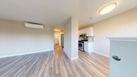 This thoughtfully designed 1-bedroom, 1-bathroom residence offers a comfortable and efficient single-floor layout. Light-toned laminate flooring runs consistently throughout the home, creating a cohesive and clean aesthetic. The open living area features a wall-mounted mini-split climate control unit and flows naturally toward the kitchen, which is outfitted with stainless steel appliances including a gas range, microwave, and refrigerator. White shaker-style cabinetry and built-in open shelving provide ample storage, complemented by a neutral countertop and a stainless steel sink. The bedroom is a well-proportioned private retreat featuring a sliding glass door that opens to a balcony with outdoor views of surrounding trees, as well as a large window fitted with blinds for natural light control. A sliding mirrored closet offers generous built-in storage. The bathroom includes a full tub-shower combination with classic bronze fixtures and a small window for ventilation. A dedicated laundry area houses a stacked washer and dryer unit, adding everyday convenience. Warm, neutral wall tones and consistent flooring tie the entire space together with a modern, move-in-ready feel.