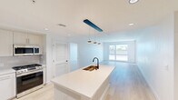 This thoughtfully designed 2-bedroom, 3-bathroom residence offers a clean, modern aesthetic across a single floor. Light hardwood flooring flows seamlessly throughout, complementing the crisp white walls and creating a bright, cohesive feel.

The open-concept kitchen and living area forms the heart of the home. The kitchen is outfitted with flat-front white cabinetry, a light gray tile backsplash, stainless steel appliances including a gas range, microwave, and a full-size side-by-side refrigerator, and a large central island with a quartz countertop and matte black fixtures. Pendant lighting with a bold blue accent rail adds a stylish focal point overhead. The living area flows naturally from the kitchen and is bathed in natural light from a large sliding glass door that opens to an outdoor space.

The spacious primary bedroom features a sliding glass door with outdoor views, two dedicated closets, and direct access to a well-appointed en-suite bathroom. The primary bath includes a dual-sink vanity with illuminated mirrors, quartz countertops, and matte black hardware. A second bedroom offers generous proportions and ample natural light. The additional bathrooms feature clean white finishes with a soaking tub, matte black fixtures, and light wood-style flooring throughout.