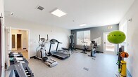 This single-floor fitness center on Central Avenue in Chattanooga, Tennessee offers a well-equipped space designed to support a complete workout routine. The main exercise area features a clean, open layout with durable speckled flooring and a neutral color palette of white and grey tones, creating a bright and focused environment. The room is illuminated by flush-mounted panel lighting in the ceiling, complemented by natural light streaming through slatted blinds on the windows. Cardio equipment includes a treadmill, elliptical trainer, stationary exercise bike, and a multi-station cable machine, providing a well-rounded selection for both aerobic and resistance training. A stability ball and weight bench round out the functional training options. A dedicated free-weight area houses a tiered dumbbell rack stocked with a range of weights, alongside posted fitness center rules for user reference. The facility also includes a separate restroom area with a walk-in shower finished in large-format, light grey porcelain tile and brushed nickel fixtures, offering a polished and practical post-workout amenity. Connected hallways and multiple entry points allow for smooth circulation throughout the space. Overall, this fitness center delivers a practical, well-maintained environment suited for everyday exercise needs.