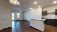 Located at 1530 Marbach Oaks in San Antonio, Texas, this single-floor unit offers a well-designed open layout that seamlessly connects the main living areas. Rich, dark hardwood-style flooring runs throughout the space, lending warmth and continuity to every room.

The living area is bright and welcoming, featuring a ceiling fan with light kit, a glass-panel door leading to a private balcony, and adjacent windows fitted with blinds that allow natural light to fill the space. The open-concept design flows directly into the kitchen, which is appointed with dark cabinetry, granite-style countertops, a full suite of black appliances including a refrigerator, range, microwave, and dishwasher, and a central island that provides additional prep and seating space.

The bedrooms continue the hardwood-style flooring and are equipped with ceiling fans and multiple windows offering outdoor views and ample natural light. The primary bathroom features a dark vanity with a granite-style countertop and direct access to a walk-in closet, adding practical storage to the suite.

Neutral-toned walls throughout the unit create a clean, versatile backdrop. The thoughtful layout, quality finishes, and abundance of natural light make this a functional and inviting living space in San Antonio's west side.