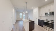 This single-floor unit showcases a thoughtfully designed open-concept layout with light-toned wood-style flooring that flows consistently throughout the space. The kitchen serves as a central highlight, anchored by a peninsula island with a granite countertop and undermount sink, illuminated by glass pendant lights. Cabinetry features a two-tone design, pairing white upper shaker-style cabinets with dark espresso lower cabinets. Stainless steel appliances, including a refrigerator, range, microwave, and dishwasher, complete the kitchen. A tiled backsplash adds a clean, polished detail.

The kitchen opens directly into a spacious living area fitted with a ceiling fan and access to an exterior door, allowing natural light to fill the room. Outdoor views of the surrounding landscape are visible through generously sized windows fitted with blinds. The bedrooms are bright and well-proportioned, each featuring ceiling fans, large windows with outdoor views, and ample wall space. The bathroom includes a granite-topped vanity with dark cabinetry, a tub-shower combination with white tile surround, and matching wood-style flooring, maintaining a cohesive aesthetic throughout the unit.