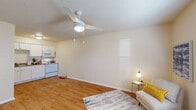 This single-story, 2-bedroom, 1-bathroom unit offers a practical and comfortable layout designed to maximize its compact footprint. The open-concept living area flows seamlessly into the kitchen, both featuring warm hardwood-style flooring that runs throughout the entire unit. The living room is bright and welcoming, with natural light filtering in through slatted blinds, a ceiling fan with integrated lighting, and neutral beige walls that create a clean, versatile backdrop. The kitchen is well-appointed with ample white cabinetry, a double-basin sink, generous counter space, and white appliances including a refrigerator, electric range, and over-the-range microwave. Both bedrooms continue the hardwood-style flooring and are each equipped with ceiling fans and windows that allow natural light to fill the rooms. The primary bedroom offers a functional closet and enough space for standard bedroom furnishings. The second bedroom, though more compact, is equally bright. The single full bathroom features a vanity with a speckled countertop, an integrated sink, and a large wall mirror. Textured ceilings are consistent throughout the unit, adding subtle character to the overall design.