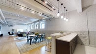 Located at 390 Capitol, this single-floor space masterfully combines industrial character with contemporary design elements. The open layout is anchored by striking exposed white-painted brick walls and soaring ceilings that reveal original wooden beams alongside modern ductwork, lending the space an authentic loft-like aesthetic.

Natural light filters through a row of arched windows along one wall, illuminating the warm hardwood floors and highlighting the textural contrast between the raw architectural elements and refined finishes. A cluster of pendant lights with cylindrical glass shades hangs over a substantial stone-topped island or bar area, supported by dark wood cabinetry, creating a functional and visually anchored focal point.

The open dining and gathering area features a wooden dining table surrounded by industrial-style metal chairs, set atop a patterned area rug that softens the overall aesthetic. Track lighting mounted to the ceiling provides additional illumination throughout the space.

The overall ambiance balances a raw, historic character with polished, modern touches, making the space well-suited for a variety of uses, from collaborative work settings to social and dining events.