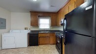 This single-floor residence in Garden Farmingdale offers a practical and comfortable layout designed for everyday living. The kitchen is a functional highlight of the home, featuring warm honey-toned wood cabinetry that extends to the ceiling, providing generous storage throughout. Dark countertops contrast nicely with the light tile flooring, while a window above the sink allows for natural light. The kitchen is fully equipped with black appliances, including a refrigerator, range, and dishwasher. Notably, an in-unit washer is conveniently located within the kitchen area, adding practical value to the space. The living areas are finished with soft wall-to-wall carpeting in a neutral tone, creating a warm and inviting atmosphere. Smooth, light-colored walls provide a clean backdrop throughout, and a ceiling fan with an integrated light fixture adds both comfort and functionality to the room. Subtle architectural details such as clean white baseboards and trim contribute to the tidy, well-maintained character of the home. Overall, the residence presents a straightforward, move-in-ready layout suited for those seeking a comfortable and efficiently designed living space in the Farmingdale area.