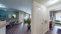 This single-story residence offers a thoughtfully designed layout encompassing three bedrooms, two bathrooms, a living room, dining room, kitchen, three hallways, and two closets. The interior is unified by durable wood-look flooring throughout the main living areas, complemented by plush carpet in the bedrooms. A striking teal accent wall anchors the living and dining spaces, adding a bold yet cohesive design element throughout.

The living room features crown molding, a ceiling fan, built-in arched display niches, and a sliding glass door opening to a private balcony with outdoor views. The adjacent dining area continues the teal palette, accented by chair rail molding. The galley-style kitchen is equipped with rich wood cabinetry, granite-style countertops, and stainless steel appliances, providing ample storage and workspace.

The primary bedroom offers a ceiling fan, a window with natural light, and a teal accent wall. The bathrooms are finished with warm wood vanities, granite-style countertops, large framed mirrors, and wood-look flooring. Multiple hallways connect the rooms efficiently, while two dedicated closets provide convenient storage throughout the residence.