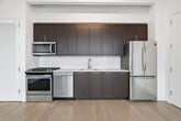 This 420 square foot apartment, located in Jamaica, New York, offers a thoughtful layout that maximizes every inch of space. The modern kitchen is the focal point, featuring sleek dark wood cabinetry that extends to the ceiling, providing ample storage. Stainless steel appliances, including a refrigerator, dishwasher, oven, and over-the-range microwave, complement the clean white countertops and backsplash. The kitchen's open design allows for easy movement and connectivity to the living area.

The bathroom showcases a contemporary aesthetic with a white subway-tiled shower/tub combination, a dark wood vanity, and a striking patterned floor. A spacious closet with built-in shelving and hanging rods offers excellent organization options. Throughout the apartment, warm wood flooring adds a touch of elegance and ties the spaces together.

Despite its compact size, the apartment feels open and airy, likely due to its efficient layout and use of light colors. The overall design aesthetic is clean and modern, appealing to those who appreciate minimalist, functional living spaces in an urban setting.