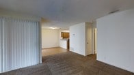 This single-floor, 1-bedroom, 1-bathroom unit offers a practical and functional layout designed for comfortable everyday living. The main living area features wall-to-wall carpeting that adds warmth underfoot, while the adjoining space transitions to hard surface flooring, providing a clear delineation between living and kitchen zones. The kitchen is open and accessible from the main living area, equipped with warm-toned wood cabinetry and a countertop workspace, along with a sink and appliances visible from the common area. A pass-through style counter connects the kitchen to the rest of the unit, making the space feel open and cohesive. The textured ceiling runs throughout the unit, adding a classic residential character. Vertical blinds near the living area suggest access to natural light through a patio or window feature. A hallway leads to the private bedroom and bathroom, offering separation from the main living spaces. Clean white walls throughout keep the interior feeling bright and neutral. This unit is well-suited for those seeking a straightforward, single-level living arrangement with clearly defined spaces and functional design.