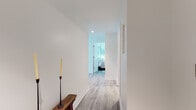 This thoughtfully designed single-floor residence offers a seamless blend of modern architecture and refined interiors. Light hardwood flooring flows consistently throughout, unifying each space with a warm, cohesive tone against a crisp all-white palette.

The open-concept kitchen serves as a functional centerpiece, featuring a large waterfall-edge island with seating for multiple bar stools, white cabinetry extending to the ceiling, stainless steel appliances, and recessed lighting overhead. Adjacent living areas are bathed in natural light through expansive floor-to-ceiling windows that frame lush outdoor greenery and urban views, creating a bright and airy atmosphere.

Both bedrooms are generously proportioned and benefit from large black-framed windows that invite abundant daylight and provide scenic outdoor views. The primary bedroom includes a dedicated vanity area, while the second bedroom features an en-suite feel with equal access to natural light.

Two bathrooms are finished with earthy stone-look tile flooring contrasted by white vanities with under-cabinet storage and clean wall-mounted fixtures, maintaining the space's contemporary character. A well-appointed hallway connects the private and shared areas of the residence, accented by a rustic wood bench that adds a subtle organic touch to the otherwise minimal design.