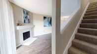 This two-story home offers a well-organized layout across both levels, blending functional design with comfortable living spaces. The main level centers around a spacious living room highlighted by a white-surround fireplace, rich dark hardwood-style flooring, and a large sliding glass door that floods the room with natural light. A staircase with carpeted treads connects seamlessly to the upper floor. Adjacent to the living area, the dining space flows directly into the kitchen, which is outfitted with a galley-style configuration featuring dark espresso cabinetry, granite-style countertops, black appliances, a stainless steel sink, and track lighting overhead. A peninsula with a partial wall separates the kitchen from the entry area, adding definition to the space. A bathroom on the lower level includes hardwood-style flooring and clean, neutral finishes. Upstairs, the bedrooms are carpeted for comfort and each features a ceiling fan with light fixture and window with blinds for natural light and privacy. An open loft-style overlook connects the upper hallway to the lower level below. Throughout the home, textured ceilings, warm neutral wall tones, and consistent trim work contribute to a cohesive and inviting atmosphere.