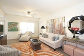 This single-story residence offers a thoughtfully arranged layout with distinct living, dining, kitchen, bedroom, and bathroom areas. The living room serves as a welcoming centerpiece, featuring carpet flooring, a ceiling fan, and natural light from a window with blinds. The space accommodates a comfortable seating arrangement anchored by a bold zebra-print area rug.

The kitchen is well-equipped with rich dark wood cabinetry extending to the upper walls, granite-style countertops, a double sink, and black appliances including a range, microwave, and refrigerator. Tile flooring runs through the kitchen and into the adjacent dining area, which comfortably fits a full dining set beneath decorative wall art.

Two bedrooms feature plush carpet, ceiling fans, windows with natural light, and closets with sliding doors. Each room offers ample space for standard bedroom furnishings. The bathrooms feature matching dark wood cabinetry, tile flooring, vanities with mirrors, and tub-shower combinations with sliding glass doors. A second, more compact bathroom includes a vanity and shower. Throughout the residence, neutral wall tones provide a versatile backdrop that complements each functional area.