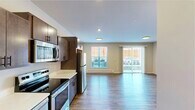 This efficiently designed single-floor unit offers a thoughtful layout that maximizes every square foot. The open-concept kitchen and living area forms the heart of the space, where the kitchen is outfitted with dark walnut-toned cabinetry, white countertops, and a full suite of stainless steel appliances — including an electric range, over-the-range microwave, dishwasher, and refrigerator. The kitchen flows seamlessly into the living area, which is bright and airy thanks to large sliding glass doors that open to an outdoor balcony, as well as an additional window fitted with horizontal blinds. Vertical blinds on the sliding door allow for flexible light control. Warm wood-look flooring runs continuously throughout the entire unit, adding a cohesive and contemporary feel. The full bathroom features a clean, modern aesthetic with a dark-cabinetry vanity, white countertop, a tub-shower combination, and matching wood-look flooring. A dedicated in-unit laundry room houses a stacked front-loading washer and dryer set, adding everyday convenience. The unit's neutral color palette, recessed and flush-mount lighting, and baseboard heating complete this well-appointed and functional living space.