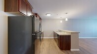 Located at 320 Allan Ave in Owatonna, Minnesota, this 1-bedroom, 1-bathroom unit offers a thoughtfully designed single-floor layout with a cohesive blend of modern finishes and functional living spaces. Light-toned luxury vinyl plank flooring flows through the open-concept kitchen and living area, creating a bright and seamless feel. The kitchen is well-equipped with rich, dark cherry wood cabinetry extending to the ceiling for ample storage, granite-look countertops, a peninsula with pendant lighting overhead, and black appliances including a full-size refrigerator, range, microwave, and dishwasher. The adjacent living area is open and airy, benefiting from natural light through a large window and private entry door. The bedroom features plush neutral carpeting and a window with views to the exterior, providing a quiet and comfortable retreat. A closet door offers convenient in-room storage. The full bathroom includes a rich wood vanity with white countertop, a large mirror, tile flooring, and a tub-shower combination. A dedicated utility room rounds out the practical offerings of this well-organized unit.