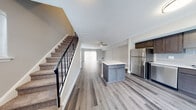 This thoughtfully designed two-story home offers a seamless blend of modern finishes and functional living spaces across both levels. The main floor greets you with an open-concept layout where the kitchen, dining, and living areas flow effortlessly together beneath a ceiling fan, all finished with durable wood-look plank flooring. The kitchen is a standout, featuring dark shaker-style cabinetry, crisp white countertops, a subway tile backsplash, a center island, and a full suite of stainless steel appliances including a refrigerator, dishwasher, microwave, and range. A sliding glass door connects the main living area to the outdoors, filling the space with natural light. A carpeted staircase with a sleek black metal railing leads to the upper level, where bedrooms are finished with plush carpet and neutral tones. The primary bedroom is generously sized with multiple windows and a large walk-in closet outfitted with wire shelving. Bathrooms are well-finished, with one featuring tile flooring, a tub-shower combination with decorative mosaic tile surround, and dark cabinetry with a white vanity top. The overall aesthetic is clean, contemporary, and move-in ready.