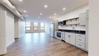 Located on the fifth floor at 8 W King Street in the heart of Lancaster, PA, Suite 507 is a thoughtfully designed, single-level unit comprising six rooms. The interior is finished in a clean, contemporary style with crisp white walls, recessed lighting, and warm wood-look tile flooring that runs consistently throughout the space.

A long, well-lit corridor welcomes you inside, leading to the open main living and kitchen area. Large windows along one wall flood the space with natural light and offer elevated views of the surrounding cityscape. The kitchen is fully equipped with stainless steel appliances — including a full-size refrigerator, range with oven, dishwasher, and microwave — complemented by shaker-style cabinetry in a soft gray finish, dark countertops, a single-basin sink, and open shelving with black metal brackets for added storage and display.

The bathroom features a shaker-style vanity with a dark stone countertop and a round mirror above, alongside a separate water closet housing a glass-enclosed walk-in shower with floor-to-ceiling marble-look tile. A dedicated utility room provides in-unit laundry with a combination washer/dryer unit and a water heater. Additional rooms offer flexible, open spaces suitable for various uses, each featuring exposed ductwork details that add an industrial character to the otherwise modern aesthetic.