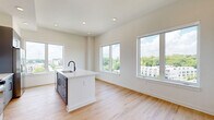 Located at 433 Bishop St NW in Atlanta's vibrant West Midtown neighborhood, this well-appointed 2-bedroom, 2-bathroom residence offers a thoughtfully designed single-floor layout. The open-concept living and kitchen area serves as the heart of the home, bathed in natural light from oversized windows that frame sweeping views of the Atlanta skyline and lush treetops. Light wood-tone flooring runs throughout the main living areas, enhancing the bright and airy atmosphere. The contemporary kitchen is a standout feature, showcasing sleek gray flat-front cabinetry extending to the ceiling, a white subway tile backsplash, stainless steel appliances including a gas range, microwave, and refrigerator, and a large white quartz island with an undermount sink and matte black faucet — ideal for both meal prep and casual dining. The living area flows seamlessly from the kitchen, offering generous space with continued views through multiple large windows. Both bedrooms are finished with plush carpet, large windows providing abundant natural light and open views, and panel-style white doors. The bathrooms continue the modern aesthetic with gray vanities, matte black hardware, and wood-look flooring. A dedicated closet provides additional storage. In-unit laundry is also included, adding to the overall convenience of this well-equipped residence.
