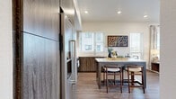 Located at 3444 S Emerson St in Englewood, CO, this thoughtfully designed one-bedroom, one-bathroom residence offers a well-appointed single-floor layout with modern finishes throughout. The kitchen is a standout feature, showcasing rich wood-grain cabinetry extending to the ceiling, stainless steel KitchenAid appliances including a full-size refrigerator, electric range, microwave, and dishwasher, complemented by crisp white countertops and a central island with bar seating. Wood-look flooring flows seamlessly through the kitchen and into the hallway, where recessed lighting and neutral walls create a clean, welcoming transition to the living areas. The living room is bathed in natural light through large windows dressed with elegant drape panels, offering views to the outdoors. The bedroom features plush carpeting, a striking accent wall with an abstract mural, a large window with balcony access, and ample closet space. The full bathroom is finished with wood-grain vanity cabinetry, a white countertop, and a glass-enclosed walk-in shower adorned with white subway tile and a hexagonal mosaic floor. In-unit laundry and a private balcony complete this polished, contemporary residence.