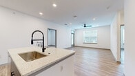 Located at 101 Dean Ave in Raymore, MO, this well-appointed 2-bedroom, 2-bathroom single-story home offers a clean, modern aesthetic with thoughtfully designed living spaces. The open-concept kitchen and living area serves as the heart of the home, featuring a large center island with quartz countertops, a deep undermount sink with a black industrial-style faucet, sleek gray cabinetry, stainless steel appliances, and a tile backsplash. Recessed lighting and a ceiling fan enhance the bright, airy feel of the connected living space, which is bathed in natural light from large windows. Durable wood-look luxury vinyl plank flooring runs consistently throughout the home, adding warmth and cohesion. The primary bedroom is generously proportioned, with multiple windows offering neighborhood views and a ceiling fan for comfort. It is complemented by a well-organized walk-in closet featuring built-in shelving and hanging rods. The primary bathroom is finished with gray vanity cabinetry, quartz countertops, black hardware accents, and a floor-to-ceiling tiled walk-in shower with a frameless glass door. The second bedroom is bright and comfortable, with a large window and clean white walls. The second bathroom mirrors the modern design of the primary. Throughout, the home maintains a crisp, neutral palette ideal for any décor style.