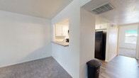 This single-floor residence offers a clean, functional layout designed for comfortable everyday living. The kitchen is outfitted with crisp white shaker-style cabinetry, speckled countertops, and black appliances including a coil-top electric range with an overhead ventilation hood and a full-size refrigerator. A pass-through window with a countertop ledge connects the kitchen to the adjacent living area, enhancing the sense of openness between spaces. The living room features plush carpeting, a wood-burning fireplace, and a sliding glass door that floods the room with natural light and provides access to an outdoor area with greenery views. A dedicated laundry area houses a full-size, top-loading GE washer and dryer side by side. The bedrooms are carpeted and well-proportioned, each featuring closet storage and natural light from windows. One room features a ceiling fan with integrated lighting and wood-look plank flooring, offering a versatile space suitable as a dining room or home office. The bathroom is clean and bright, featuring a full soaking tub with a shower, built-in shelving niches, and wood-look flooring that ties the space together. Throughout, the residence maintains a neutral, move-in-ready aesthetic with white walls and consistent finishes.