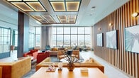 This generously scaled amenity floor offers a sophisticated, design-forward environment spread across a single level. The centerpiece is a dramatic main lounge featuring a striking coffered ceiling with embedded LED lighting panels, vertical wood-slat accent walls, and an expansive wall of floor-to-ceiling windows that frame panoramic city skyline views. Vibrant, curated furnishings in warm oranges, reds, and teals lend a contemporary and inviting atmosphere throughout.

The full-service kitchen and bar area is outfitted with sleek sage-blue cabinetry, a waterfall-edge marble island with leather bar seating, pendant tube lighting, and high-end appliances including wine coolers. Multiple dining areas offer flexible seating configurations for both intimate and group gatherings.

Additional lounge areas include a cozy retreat with arched booth seating, warm pendant lighting, and vaulted ceilings with statement fan fixtures. A sunlit corridor with terracotta hexagonal tile flooring, a living moss wall, and rattan furnishings leads to an outdoor terrace access point. A corner workspace with floor-to-ceiling glass on two sides provides sweeping city views, while a private meeting room features whimsical bird-print wallpaper and a city-facing window. Exposed brick columns and polished tile flooring unify the space with a refined urban character throughout.