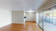 This single-floor space offers a clean, functional layout with a well-defined separation between living, sleeping, and utility areas. The open living and dining area is finished with warm hardwood-style flooring throughout and painted in neutral tones, creating a bright and versatile environment. A large sliding glass door dominates one wall, flooding the space with natural light and providing direct access to a private outdoor patio, which is enclosed by a modern slatted fence. A pendant light fixture anchors the dining area, while a wall-mounted heating unit ensures year-round comfort.

The galley-style kitchen is efficiently designed, featuring white cabinetry extending to the ceiling for ample storage, dark granite countertops, a stainless steel sink, and a full suite of stainless steel appliances including a range, microwave, and refrigerator. Hardwood-style flooring continues into the kitchen. In-unit laundry is conveniently located in a dedicated alcove adjacent to the kitchen.

The bedroom is carpeted and receives natural light through a window. The bathroom includes a white tiled tub-shower combination, a toilet, and a vanity topped with dark granite, consistent with the kitchen finishes.