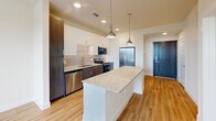 Located in Dallas, TX (75237), this thoughtfully designed single-floor residence offers a cohesive modern aesthetic with warm hardwood-style flooring and a neutral color palette carried throughout every room. The kitchen serves as a standout centerpiece, featuring a granite-topped island illuminated by pendant lighting, two-tone cabinetry with white upper cabinets and dark lower cabinets, a textured tile backsplash, and a full suite of stainless steel appliances including a refrigerator, range, microwave, and dishwasher. The layout flows efficiently from the kitchen toward the bedroom and bathroom areas. The bedroom is a bright, comfortable retreat with a ceiling fan, a window dressed with blinds that invite natural light and outdoor views, and direct access to the dedicated closet. The walk-in closet is outfitted with dual hanging rods and multiple shelving tiers, providing well-organized storage. The bathroom continues the home's refined design language with a dark wood vanity, granite countertop, framed mirror, and chrome fixtures. Consistent warm-toned flooring and clean white walls unify the space, resulting in a residence that is both functional and visually cohesive.