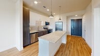 Located in Dallas, TX (75237), this thoughtfully designed single-floor residence offers a cohesive modern aesthetic with warm hardwood-style flooring and a neutral color palette carried throughout every room. The kitchen serves as a standout centerpiece, featuring a granite-topped island illuminated by pendant lighting, two-tone cabinetry with white upper cabinets and dark lower cabinets, a textured tile backsplash, and a full suite of stainless steel appliances including a refrigerator, range, microwave, and dishwasher. The layout flows efficiently from the kitchen toward the bedroom and bathroom areas. The bedroom is a bright, comfortable retreat with a ceiling fan, a window dressed with blinds that invite natural light and outdoor views, and direct access to the dedicated closet. The walk-in closet is outfitted with dual hanging rods and multiple shelving tiers, providing well-organized storage. The bathroom continues the home's refined design language with a dark wood vanity, granite countertop, framed mirror, and chrome fixtures. Consistent warm-toned flooring and clean white walls unify the space, resulting in a residence that is both functional and visually cohesive.