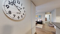 This single-floor residence offers a functional and comfortable layout across several well-defined living spaces. The entryway, accented by a large decorative wall clock, leads into an open living area finished with wood-style plank flooring and track lighting overhead. The living room is generously sized, featuring multiple windows that allow natural light to fill the space, along with a glass-paned exterior door providing additional brightness and outdoor access.

The galley-style kitchen runs parallel along one side and is equipped with warm honey-toned cabinetry, grey laminate countertops, a double sink, and black appliances including a refrigerator, electric range, built-in microwave, and dishwasher. Light wood-style flooring carries through the kitchen as well.

Both bedrooms are carpeted and comfortably scaled, each offering closet storage. One bedroom features a window with a view of surrounding greenery and a reach-in closet with built-in shelving. The two bathrooms are similarly appointed, each with a wood-tone vanity, tile surround tub-shower combination, and wood-style flooring. One bathroom includes a window for added ventilation. A dedicated laundry area houses a full-sized top-load washer with overhead wire shelving, completing this practical and cohesive residence.
