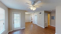 This single-story, 1-bedroom, 1-bathroom unit offers a practical and well-organized layout. The living area is a welcoming space anchored by wood-look flooring and a ceiling fan with an integrated light fixture, providing both comfort and functionality. A door with sidelights allows natural light to filter in, contributing to an open and airy feel. Neutral-toned walls and textured ceilings are consistent throughout the unit, creating a cohesive aesthetic.

The kitchen is efficiently designed with wood-finish upper cabinetry, white appliances including a gas range, over-the-range microwave, refrigerator, and dishwasher. Wood-look flooring continues here, and a door leads to an adjoining storage or utility area. The bedroom features plush carpeting, a window with blinds for natural light, and ample wall space for furniture placement.

The full bathroom includes a single-sink vanity with storage, a medicine cabinet with mirror, and a tub-shower combination. A hallway connects the primary living spaces and includes access to a utility panel. Overall, the unit offers a straightforward, comfortable layout with consistent finishes throughout.
