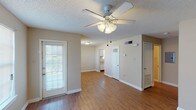 This single-story, 1-bedroom, 1-bathroom unit offers a practical and well-organized layout. The living area is a welcoming space anchored by wood-look flooring and a ceiling fan with an integrated light fixture, providing both comfort and functionality. A door with sidelights allows natural light to filter in, contributing to an open and airy feel. Neutral-toned walls and textured ceilings are consistent throughout the unit, creating a cohesive aesthetic.

The kitchen is efficiently designed with wood-finish upper cabinetry, white appliances including a gas range, over-the-range microwave, refrigerator, and dishwasher. Wood-look flooring continues here, and a door leads to an adjoining storage or utility area. The bedroom features plush carpeting, a window with blinds for natural light, and ample wall space for furniture placement.

The full bathroom includes a single-sink vanity with storage, a medicine cabinet with mirror, and a tub-shower combination. A hallway connects the primary living spaces and includes access to a utility panel. Overall, the unit offers a straightforward, comfortable layout with consistent finishes throughout.