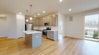 This well-appointed single-floor residence offers a thoughtfully designed open-concept layout that seamlessly connects the kitchen and living areas. The kitchen is a standout feature, showcasing warm taupe shaker-style cabinetry extending to the ceiling, crisp white quartz countertops, a subway tile backsplash, and a full suite of stainless steel appliances including a gas range, built-in microwave, and refrigerator. A central kitchen island with an integrated sink and pendant lighting above adds both functionality and style. Light-toned hardwood flooring runs throughout, enhancing the bright, airy atmosphere created by recessed lighting and natural light from large windows. The space includes two well-sized bedrooms, each featuring a closet and windows with views of the surrounding community. Two bathrooms provide comfort and practicality — one featuring a glass-enclosed walk-in shower with elegant tile surround and rich walnut-toned cabinetry, and the other offering a full tub/shower combination with coordinating finishes. A dedicated laundry area accommodates a stacked washer and dryer unit, adding everyday convenience. Overall, the residence presents a clean, contemporary aesthetic with quality finishes throughout.