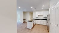 Located at 6801 W Friendly Ave in Greensboro, NC, this single-floor 2-bedroom, 2-bathroom residence offers a clean, modern aesthetic throughout. The open-concept kitchen and living area serves as the heart of the home, featuring crisp white shaker cabinetry, dark granite countertops, a peninsula island, and a full suite of stainless steel appliances — including a refrigerator, range, microwave, and dishwasher — all set atop warm light wood-style flooring. The living area is bright and airy, with a ceiling fan and French doors that invite natural light and provide outdoor access. Both bedrooms are carpeted and equipped with ceiling fans; the primary bedroom is generously sized, with dual closets — including a walk-in — and large windows that bring in natural light. The primary bathroom features a double-sink vanity with dark granite countertops, white cabinetry, and wood-style flooring. The second bathroom offers a single vanity with matching finishes and a shower-tub combination. A dedicated laundry room with side-by-side washer and dryer and wire shelving adds everyday convenience. The hallway connects all rooms with a cohesive, neutral palette throughout.