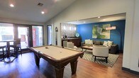 This single-floor recreational lounge is thoughtfully designed to serve as a social hub for leisure and entertainment. The main area is anchored by a full-size billiards table set atop rich hardwood flooring, offering a classic focal point for game nights and casual gatherings. Vaulted ceilings add a sense of openness to the space, while recessed lighting ensures a well-lit environment throughout.

Adjacent to the game area, a wet bar station is finished with a mosaic tile backsplash and pendant lighting, providing a convenient refreshment setup complete with a coffee maker and mini-refrigerator. A Coca-Cola vending machine near the entrance adds a fun, casual touch to the space.

The lounge area features a cozy seating arrangement with patterned armchairs and a sofa grouped around a central coffee table on a geometric-patterned area rug. A bold blue accent wall serves as a vibrant backdrop, complemented by a large abstract artwork in green and neutral tones. Together, these design elements create a space that is both visually dynamic and functionally versatile, ideal for relaxation and social interaction.