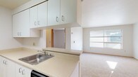 This single-floor unit offers a clean, functional layout designed for comfortable everyday living. The open-concept living area is bright and inviting, with natural light streaming through a large window fitted with horizontal blinds and reflecting off the neutral, wall-to-wall carpeting. A ceiling fan adds to the room's comfort and airflow.

The kitchen is thoughtfully designed in a galley style, featuring white cabinetry that extends to the ceiling for ample storage, light-toned laminate countertops, a stainless steel sink, a white electric range, a full-size refrigerator, and a dishwasher. The tile flooring in the kitchen provides a practical contrast to the carpeted living spaces. A peninsula counter connects the kitchen to the living area, creating an efficient pass-through layout. A closeted pantry or utility area is accessible directly from the kitchen.

The bedroom is generously sized with soft carpet, neutral walls, and a wide sliding-door closet fitted with built-in shelving for organized storage. A window allows natural light to fill the space.

The bathroom includes a full soaking tub and shower combination with smooth, neutral-toned surround walls and chrome fixtures, maintaining a simple and clean aesthetic throughout. The unit's consistent use of light tones and practical finishes creates a cohesive, move-in-ready environment.
