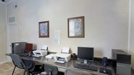 This single-floor business center is designed to meet the practical needs of guests and professionals alike. The space is anchored by a granite-topped workstation desk that runs along the wall, providing ample surface area for multiple users simultaneously. The setup includes desktop computers with full keyboards, as well as several HP inkjet printers, ensuring that printing and computing needs are readily accommodated.

The room features neutral, light-colored walls that contribute to a clean and focused atmosphere. Two decorative framed vintage world map prints are displayed on the wall above the workstations, adding a subtle touch of character to an otherwise utilitarian space. Ergonomic task chairs are positioned at each workstation, offering comfort during extended use.

The overall ambiance is professional and efficient, with a layout optimized for productivity. Adequate lighting illuminates the work surfaces, and the compact yet well-organized arrangement makes the most of the available space. This business center serves as a convenient resource for anyone requiring access to computing or printing facilities, combining essential technology with a tidy and orderly environment.
