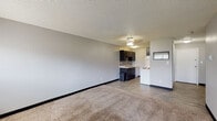 Located at 370 N Murray Blvd in Colorado Springs, Colorado, this single-floor unit offers a practical and functional layout well-suited for comfortable everyday living. The open living area is generously sized, featuring neutral gray walls, plush wall-to-wall carpeting, and a textured ceiling. The space transitions seamlessly to hard-surface flooring as it approaches the kitchen, providing a clear delineation between living and cooking areas. A window allows natural light to fill the room, complemented by a ceiling light fixture overhead.

The galley-style kitchen is efficiently designed, featuring dark espresso cabinetry on both sides, a mosaic tile backsplash, light-toned countertops, a double-basin stainless steel sink, and white appliances including a refrigerator and a coil-top electric range with overhead ventilation.

The bedroom is a well-proportioned, carpeted room with soft gray walls, a textured ceiling, and a louvered bifold closet door providing ample storage with open shelving. A window brings in natural light and views of the surrounding greenery, with a baseboard heater situated beneath it.

The bathroom features a full-size soaking tub and shower combination with clean white subway tile surround, wood-look vinyl flooring, and chrome fixtures, offering a simple and functional design.