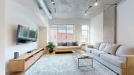 Located at 951 Fell St in Baltimore, MD, this urban loft showcases a striking blend of industrial and contemporary design across a single floor. The expansive living area commands attention with soaring exposed concrete ceilings, visible ductwork, and track lighting that emphasize the space's loft-style character. Large windows flood the room with natural light while offering views of the surrounding neighborhood, complementing the warm hardwood flooring beneath. Exposed concrete columns punctuate the living space, adding to the raw, architectural aesthetic.

The kitchen is well-appointed with warm wood cabinetry, dark granite countertops, stainless steel appliances, and hardwood flooring that continues seamlessly from the living area. An arched architectural detail adds a subtle decorative touch.

The bedrooms maintain the industrial aesthetic with exposed concrete ceilings and generous windows. One bedroom features a spacious walk-in closet with extensive shelving. The bathroom is finished with slate tile flooring, rich wood cabinetry, dark granite countertops, and a tiled tub-shower combination, delivering a polished, upscale feel. Throughout, the space balances raw urban elements with refined modern touches.