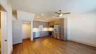 This two-story space showcases a contemporary design with clean lines and a neutral palette throughout. The kitchen serves as a central highlight, featuring wood-grain cabinetry extending to ceiling height, a textured tile backsplash, and a full suite of stainless steel appliances including a French door refrigerator, range, built-in microwave, and dishwasher. Warm hardwood-style flooring flows through the kitchen and living areas, complemented by recessed lighting and a modern ceiling fan. A barn-style sliding door adds a functional, stylish touch near the kitchen entry.

The bathrooms are finished with a cohesive warm wood-toned vanity cabinetry, white quartz countertops, and light tile flooring. The full bathroom includes a soaking tub with full subway tile surround and brushed nickel fixtures, while an additional bathroom offers a streamlined vanity with framed mirror.

The bedroom features plush neutral carpeting, two windows inviting ample natural light, and a ceiling fan for comfort. A staircase connects the two floors, visible in the layout scan, reinforcing the multi-level nature of this well-appointed space with modern finishes throughout.