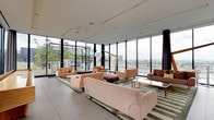 Located at 800 P Street NW in Washington D.C., this sophisticated amenity floor offers residents a refined environment for relaxation and entertainment. The expansive lounge area is defined by floor-to-ceiling glass curtain walls on multiple sides, flooding the space with natural light and providing unobstructed panoramic views of the D.C. skyline and a rooftop pool terrace. Stylish seating arrangements featuring blush and earth-toned sofas, patterned area rugs, and sculptural floor lamps create a welcoming, upscale atmosphere throughout.

Adjacent to the lounge, the gourmet kitchen is a standout feature, outfitted with professional-grade stainless steel appliances including a gas range, wall oven, wine refrigerator, and dual-basin sink. Striking amber-tinted mirror cabinetry adds a bold design element, while a long white quartz island with integrated bar seating makes the space equally suited for casual gatherings or catered events. The large-format tile flooring runs consistently throughout, contributing to a clean, cohesive aesthetic.

The dollhouse view reveals the full layout, which also includes a vibrant mural wall and a shuffleboard table, reinforcing the space's versatility as a social hub. The combination of modern design, premium finishes, and commanding city views makes this amenity floor a truly distinctive urban retreat.