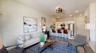 This single-floor residence is designed around an open-concept layout that seamlessly connects the kitchen, dining, and living areas. The kitchen serves as a central hub, featuring white cabinetry, granite countertops, stainless steel appliances including a refrigerator, microwave, and range, and a large island with built-in shelving and an undermount sink. Pendant lighting above the island adds both function and visual interest, while bar-height seating provides a casual dining option.

The living area extends naturally from the kitchen, highlighted by wood-style flooring, a ceiling fan, and a sliding glass door that opens onto a private balcony with outdoor views. Natural light flows freely through large windows and the glass door, creating a bright and welcoming atmosphere throughout the shared spaces.

The bedroom is carpeted for comfort and features large windows dressed with layered blinds and curtains, allowing for both light control and privacy. An en-suite bathroom connects to the bedroom, offering a glass-enclosed shower, dual vanity with granite surfaces, and white cabinetry. A spacious walk-in closet with built-in shelving and hanging rods provides generous storage. The overall aesthetic is clean and contemporary, with neutral tones throughout.