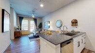 This single-floor residence offers a thoughtfully designed open-concept layout that seamlessly connects the kitchen, dining, and living areas. The kitchen is outfitted with white shaker-style cabinetry, dark granite countertops, a subway tile backsplash, and a full suite of stainless steel appliances, including a refrigerator, electric range, and built-in microwave. A peninsula with an undermount sink and additional counter space provides a natural boundary between the kitchen and the living area, which features wood-style plank flooring throughout. The living room is bright and inviting, benefiting from natural light through large windows and French doors that open to an outdoor balcony, complemented by a ceiling fan overhead. The bedroom is carpeted and well-lit by a large window, offering a comfortable and quiet retreat. An attached bathroom features a glass-enclosed walk-in shower, wood-style flooring, white cabinetry with granite countertops, and direct access to a walk-in closet with built-in shelving and hanging rods. A dedicated laundry area houses a full-sized top-load washer and dryer, adding everyday convenience to the unit.