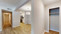 Located at 1000 Belmont Park Dr SE in Smyrna, Georgia, this single-floor residence offers a well-organized layout with a neutral color palette and consistent wood-look flooring throughout the main living areas. The galley-style kitchen is outfitted with white shaker cabinetry, light quartz countertops, a tile backsplash, and stainless steel appliances including a range, dishwasher, and refrigerator. A pendant light fixture illuminates the transition from the dining area into the kitchen, lending a welcoming ambiance to the space. The living area is bright and open, featuring a sliding glass door that leads to a private balcony overlooking a natural, wooded backdrop. A long hallway with wood-look flooring connects the main living spaces to the private quarters. The bedrooms are carpeted for comfort and each features a window that brings in natural light. The primary bedroom includes access to a generously sized walk-in closet with wire shelving and an additional storage area. The bathroom is clean and functional, featuring a white vanity with ample counter space, a medicine cabinet mirror, and a tiled tub-shower combination. Textured ceilings are present throughout, adding a classic residential character to the space.
