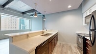 Located at 2828 Euclid Avenue in the heart of Cleveland, Ohio, this three-bedroom, three-bathroom unit offers a modern urban living experience with an industrial-chic aesthetic. The open layout makes efficient use of space across a single floor, blending contemporary finishes with functional design throughout.

The kitchen is a standout feature, boasting rich dark cabinetry, light stone countertops, a double-basin stainless steel sink, pendant lighting, and stainless steel appliances including a refrigerator, range, and dishwasher. Light wood-look flooring and exposed ductwork on the ceiling add an urban loft character to the space.

The living area is bright and airy, featuring large floor-to-ceiling windows that flood the room with natural light and frame impressive views of the Cleveland cityscape. Exposed structural beams and visible HVAC ductwork reinforce the industrial design theme.

The three bedrooms are carpeted with patterned flooring and neutral-toned walls. The primary bedroom includes a closet with double doors and windows offering outdoor views. The additional bedrooms are well-proportioned and versatile.

The three bathrooms are finished consistently with dark wood vanities, white countertops, and wood-look tile flooring. Two feature walk-in showers, while one includes a full tub-shower combination, catering to a variety of preferences.