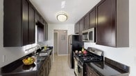 Located at 290 New Chalet Rd in Mohegan Lake, NY, this single-floor 2-bedroom, 2-bathroom residence offers a well-designed layout with thoughtful finishes throughout. The galley-style kitchen is a standout feature, showcasing rich dark espresso cabinetry extending to the ceiling, dark granite countertops, light ceramic tile flooring, and a full suite of stainless steel appliances including a gas range, built-in microwave, and refrigerator. Multiple windows allow natural light to brighten the space, creating a clean and functional cooking environment. The spacious living area is carpeted in a neutral tone and features a fireplace with a classic white mantel as a focal point, complemented by a large sliding glass door that invites additional natural light. The open layout offers generous room for flexible furniture arrangements. Both bedrooms are carpeted and well-proportioned, with ample closet space visible in the primary bedroom. The two bathrooms are finished with dark-framed vanity mirrors, white countertop sinks, dark cabinetry, and tile flooring, providing a cohesive and modern aesthetic. The overall design palette—neutral walls, dark accents, and consistent flooring choices—creates a clean, contemporary ambiance throughout the home.