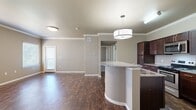 This thoughtfully designed single-story residence offers a comfortable and functional layout across one floor. The open-concept living and kitchen area serves as the heart of the home, featuring rich dark hardwood-style flooring, neutral taupe walls, and crown molding that adds a polished touch. Multiple windows with blinds invite generous natural light throughout the space, while a glass-paneled entry door enhances the bright, airy atmosphere.

The kitchen is well-equipped with dark espresso cabinetry, granite countertops, a tile backsplash, and a full suite of stainless steel appliances including a range, microwave, and refrigerator. A curved kitchen island with a pendant light overhead provides additional prep space and casual seating.

The bedroom is a comfortable retreat finished with plush carpeting, a ceiling fan with light, and a window overlooking the exterior. An adjacent walk-in closet offers ample storage with wire shelving and hanging rods on multiple walls.

The bathroom is clean and functional, featuring granite countertops with dark cabinetry, a full tub and shower with white tile surround, and matching dark hardwood-style flooring. A hallway connects all areas seamlessly, completing this well-organized and move-in-ready residence.
