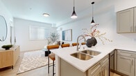 Located in Vancouver, WA, this thoughtfully designed one-bedroom, one-bathroom residence offers a clean, modern aesthetic with a cohesive layout across a single floor. Light wood flooring flows throughout the space, complementing the bright white walls and creating an airy, welcoming atmosphere. The open-concept kitchen and living area serves as the heart of the home, anchored by a spacious island with white quartz countertops, a double stainless steel sink, and seating for multiple bar stools. Gray shaker-style cabinetry lines the kitchen walls, paired with stainless steel appliances including a range and refrigerator. Sleek pendant lighting adds a modern touch above the island. The living room receives ample natural light through large windows with horizontal blinds, and features a wall-mounted mini-split system. The generously sized bedroom offers a large window, light wood flooring, and access to a walk-in closet with built-in wire shelving. The bathroom features a gray shaker vanity with white quartz countertop and a large mirror. A dedicated entryway nook with additional storage rounds out this well-appointed residence.