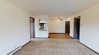 This single-floor residence offers a practical and comfortable layout designed for everyday living. The spacious living area is finished with plush carpeting and features a ceiling fan, creating a relaxed atmosphere. A sliding glass door leads to a private balcony, filling the room with natural light and providing outdoor views of the surrounding greenery. The living space flows seamlessly into the dining area, which transitions to the kitchen via a convenient pass-through window. The kitchen is thoughtfully designed in a U-shape, featuring white cabinetry with wood-tone accents, ample counter space, a double-basin sink, and a full suite of appliances including a refrigerator, electric range, built-in microwave, and dishwasher. Wood-look flooring adds warmth underfoot. The unit includes two generously sized bedrooms, each finished with soft carpeting, baseboard heating, and sliding windows that bring in natural light and outdoor views. The primary bedroom offers direct access to an en-suite bathroom and a closet, while a second full bathroom serves the rest of the unit. Both bathrooms are equipped with a tub-shower combination. Dark wood-trim doors and baseboards throughout provide consistent, cohesive detailing across the entire space.