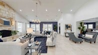 This expansive single-story space offers a thoughtfully designed open-concept floor plan that seamlessly connects the living room, dining room, and kitchen into one generous, flowing area. Soaring vaulted and tray ceilings throughout lend an impressive sense of height and grandeur, while large windows invite abundant natural light across the light-toned tile flooring that runs continuously through the space.

The main living area is anchored by a dramatic navy blue accent wall and complemented by a stylish chandelier, recessed lighting, and a stone fireplace that adds warmth and texture. The kitchen features white cabinetry, stainless steel appliances, white countertops, and a bold blue tile backsplash, with a direct sightline to the dining area. The dining room is distinguished by an elegant tray ceiling with crown molding and a chandelier centerpiece.

The hallway connects the various areas with graceful arched doorways and clean white walls, creating smooth transitions throughout. A dedicated exercise room adds functional versatility to the layout. The primary bedroom provides a comfortable and well-proportioned private retreat. Throughout the space, a cohesive navy, white, and neutral palette delivers a sophisticated, contemporary aesthetic with a welcoming ambiance.